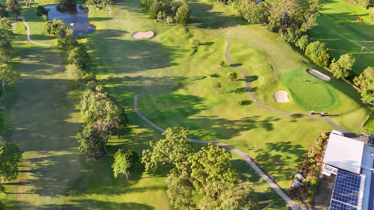 Drone footage captures a lush golf course with vibrant greens, sand bunkers, and a clubhouse under clear skies