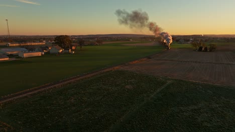 drone view of a steam engine approaching blowing smoke at sunrise traveling thru the farmlands on fall morning