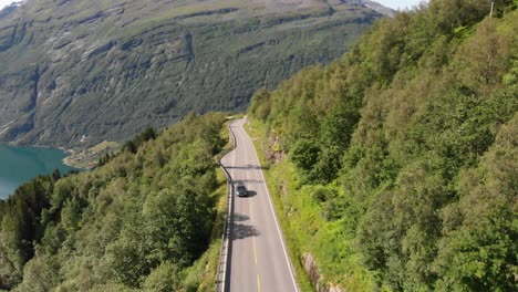 A-car-and-a-bus-drive-on-a-road-in-front-of-the-Geirangerfjord-in-Norway
