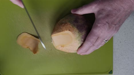 pelar un gran nabo sueco en una tabla de cortar verde por un anciano