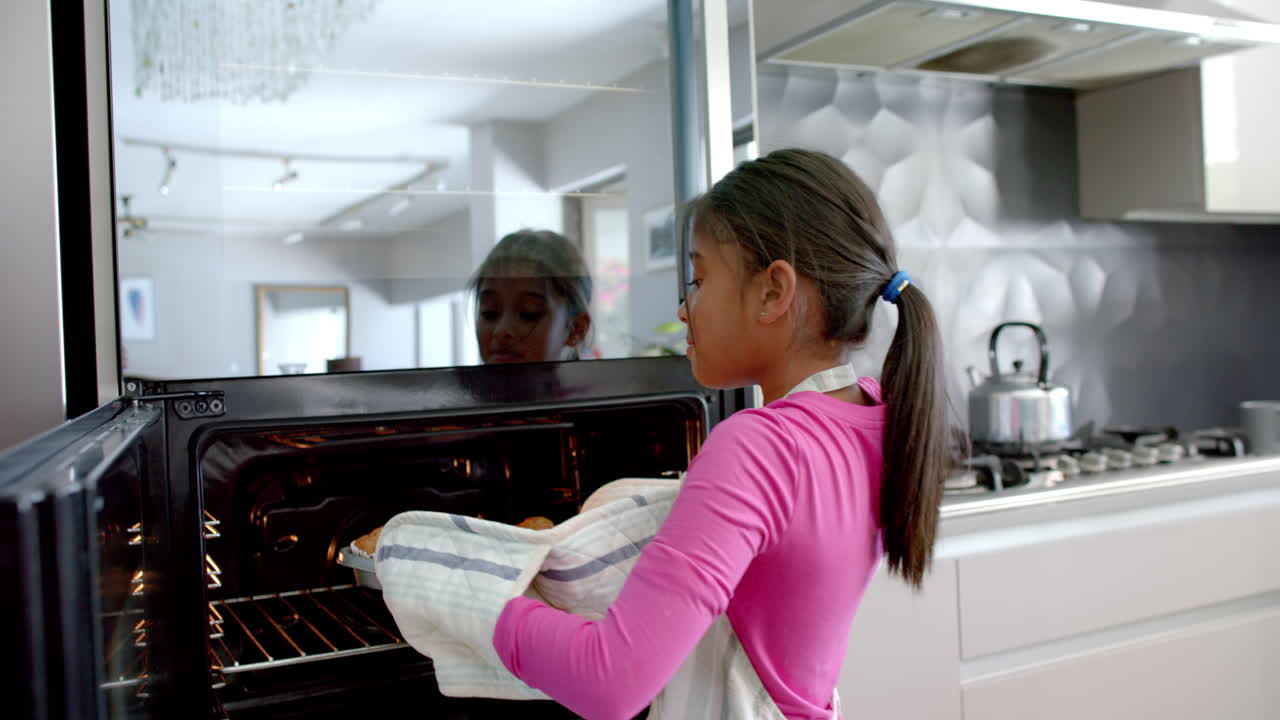 Ragazza birazziale felice che inforna in cucina, tira fuori i dolci dal forno, al rallentatore.