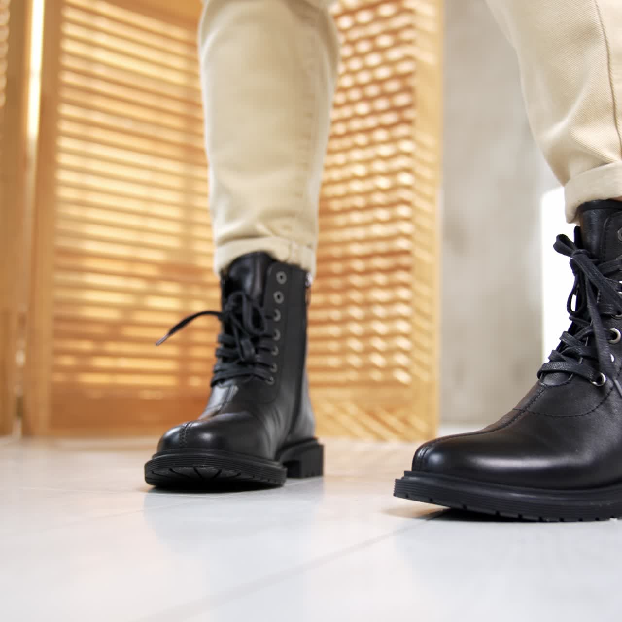 Stylish low black leather boots with laces and rounded nosepieces. Model wearing light jeans demonstrates fashionable footwear in studio. Close up