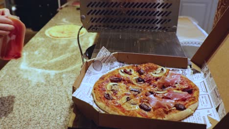 a pizza chef adds prosciutto to the top of a freshly baked pizza before sending it out for delivery