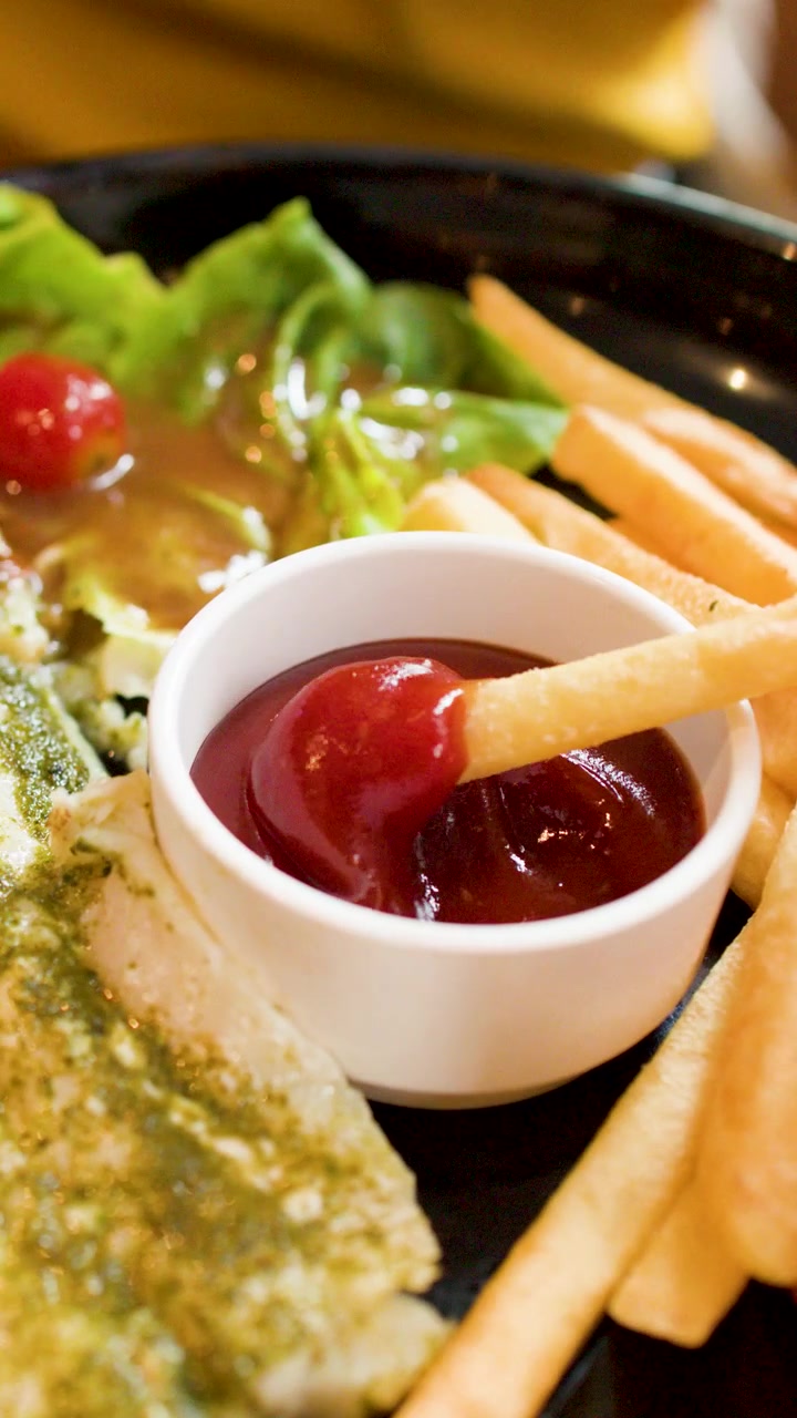 Primo piano di una mano che intinge una patatina fritta croccante in una ciotola di ketchup.