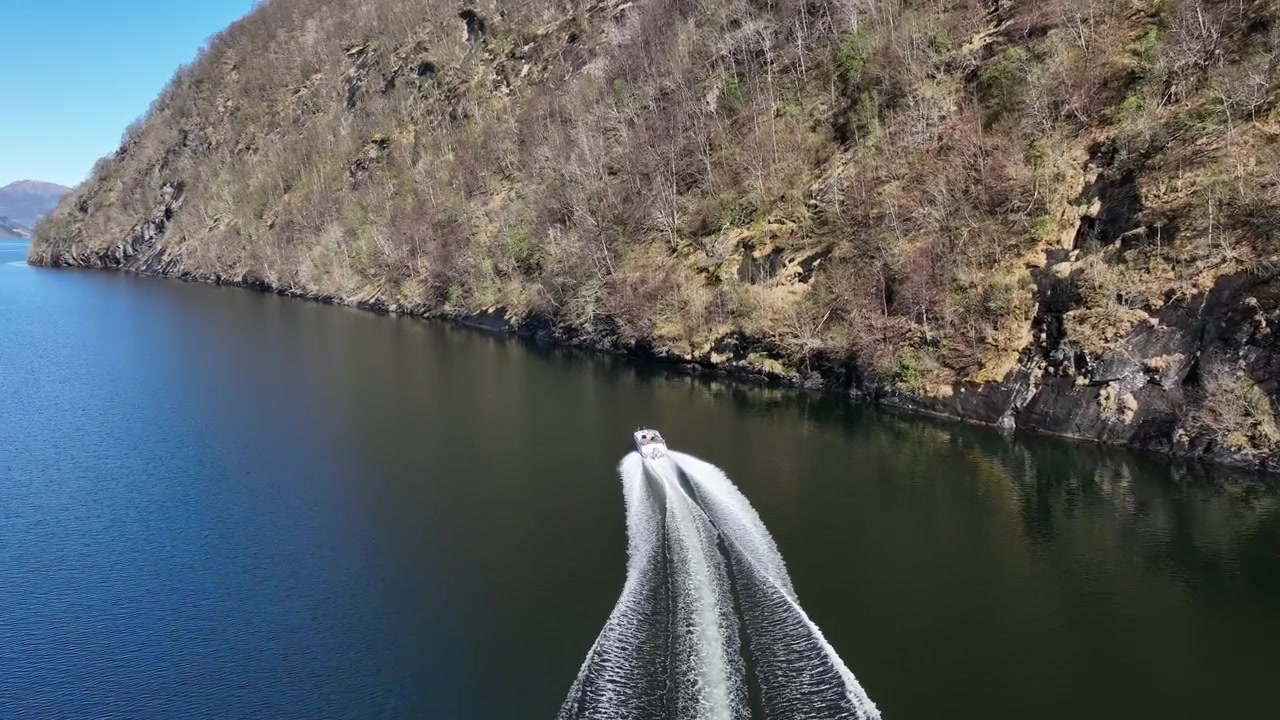Boat cruising along steep fjord cliff in Norway with wake on calm spring water