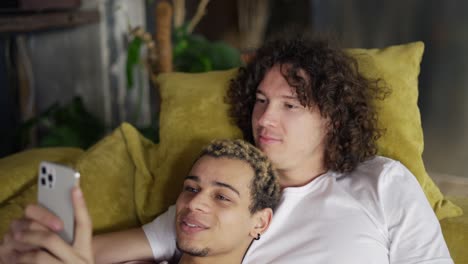 male romantic gay couple relaxing on the couch, watching the smartphone screen, close up