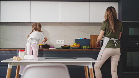 mother with little daughter cooks dinner in modern kitchen