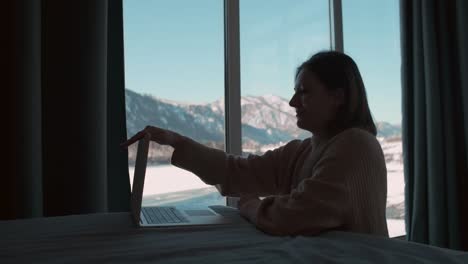 a woman works from home sitting in the bedroom by the window