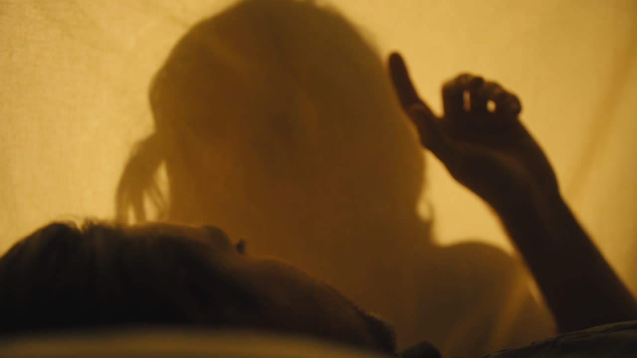 Silhouette of woman backlit on muslin while man lays on other side