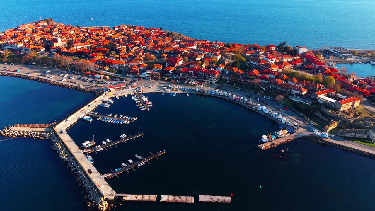 Fiskehamn i Nessebar, Bulgarien. Drönarvy över en krökt småbåtshamn fylld med små båtar, omgiven av rödtakiga byggnader i gamla stan