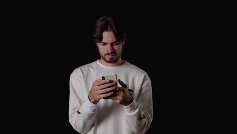 trendy young man using and typing annoyed on phone, wide, black background