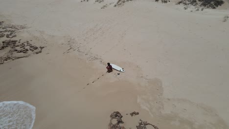 joven surfista sentada en la playa mirando pensando ir a surfear en las olas del océano pacífico en una playa de arena cerca de exmouth, australia occidental