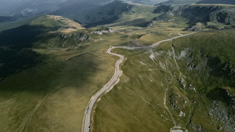 Perspectiva-Aérea-De-La-Carretera-Transalpina-En-Rumania,-Que-Revela-Su-Camino-Serpenteante-A-Través-De-Exuberantes-Terrenos-Verdes,-Bosques-Sombreados-Y-Bordes-Montañosos-Escarpados.