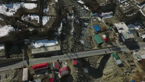 drone flying overhead above bridge over dry river bed in village town in hunza valley