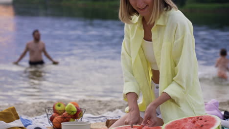 donna che taglia meloni d'acqua sulla spiaggia