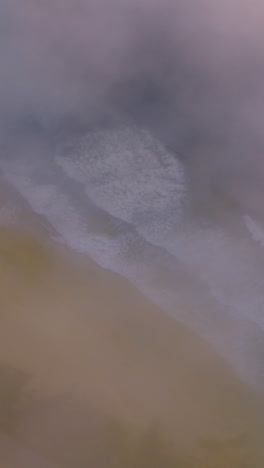 scenery of a sandy beach with beautiful foamy waves approaching. montara state beach in a thick white fog from pacific. vertical video