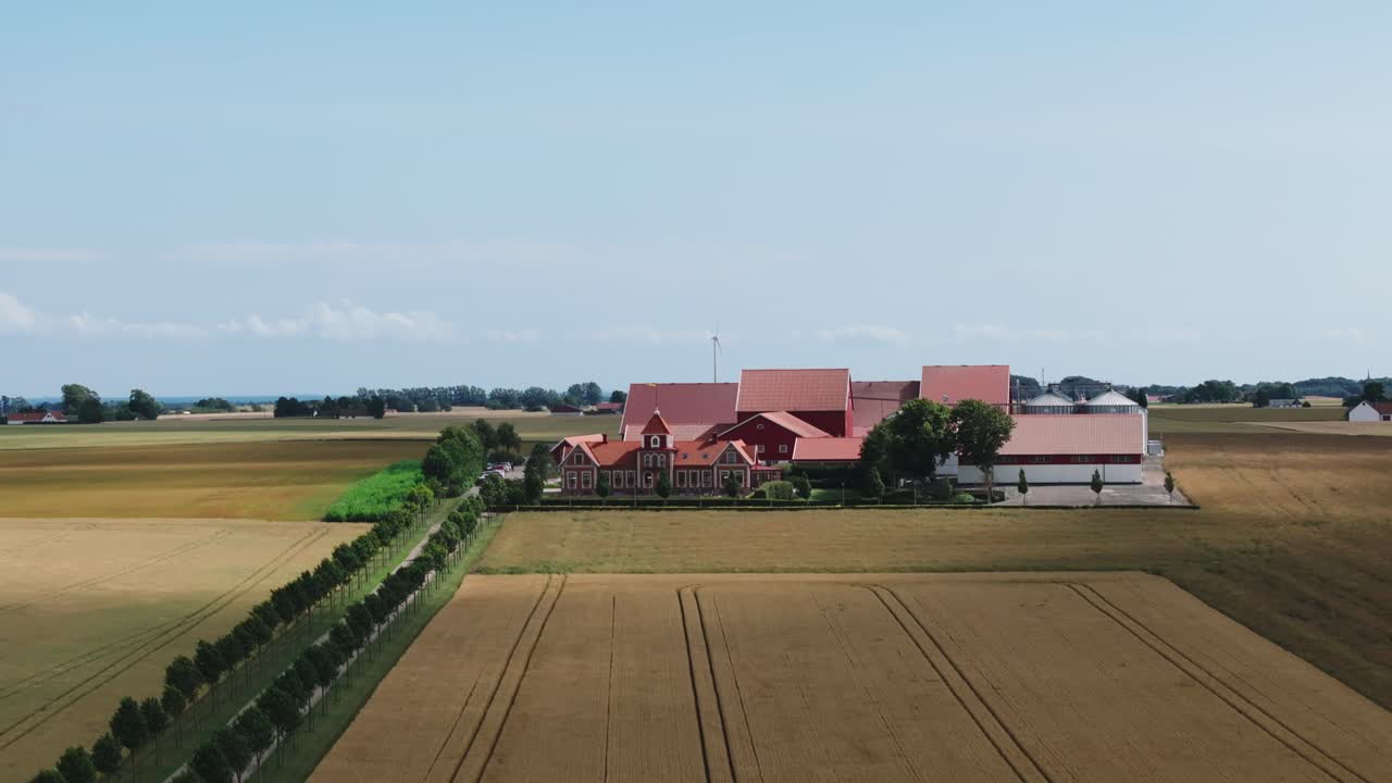 Solchi di trattore su un campo di grano con il negozio agricolo del Gunnar College in lontananza a Hammenhog, Svezia.