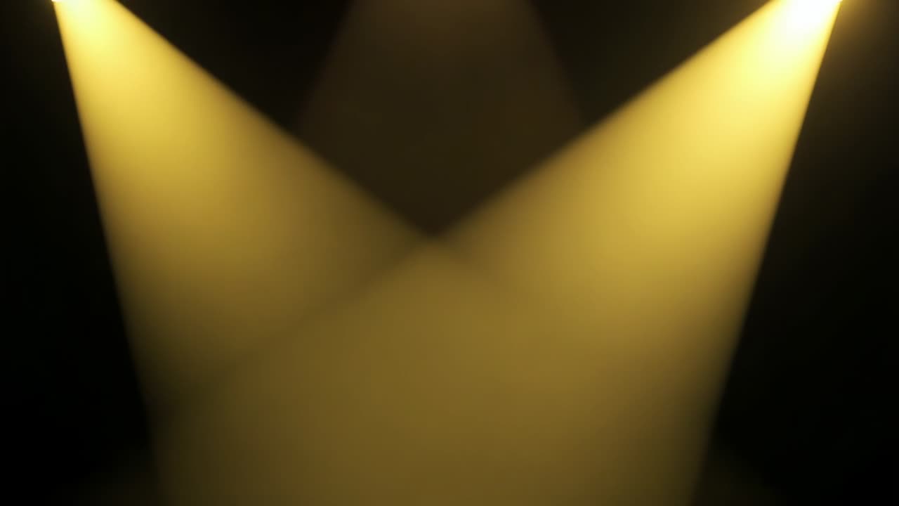 Two golden lights switching on third light joining beams converging sweeping over hazy stage floor