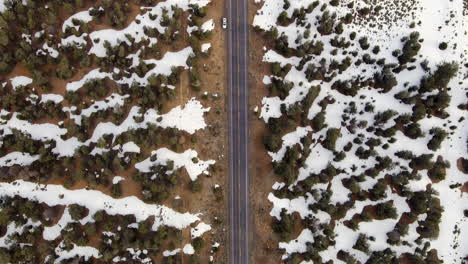 Aerial-Topdown-On-Asphalt-Road-Through-Snowy-Terrain-With-Car-Parked-On-The-Roadside