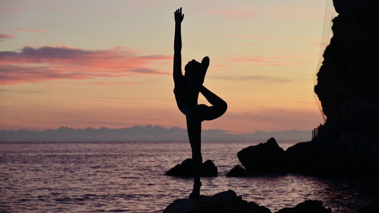 Mujer practicando yoga en una roca junto al océano durante un colorido atardecer. Budva, Montenegro