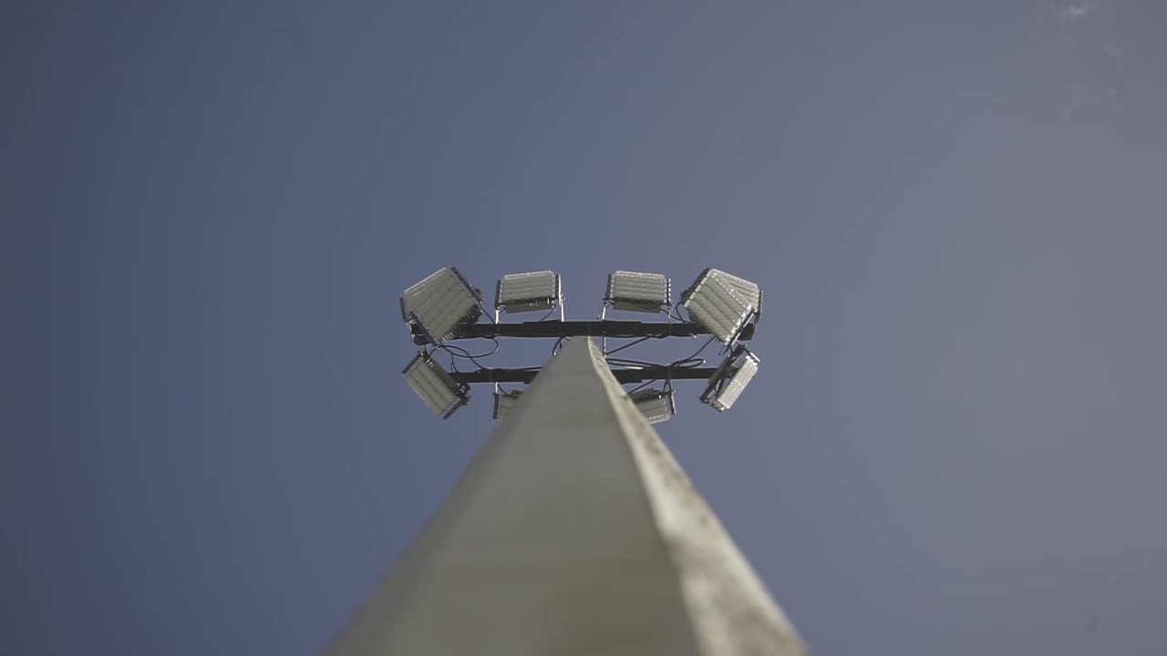 Powerful stadium lights stand tall against a clear blue sky, illuminating the vast expanse above