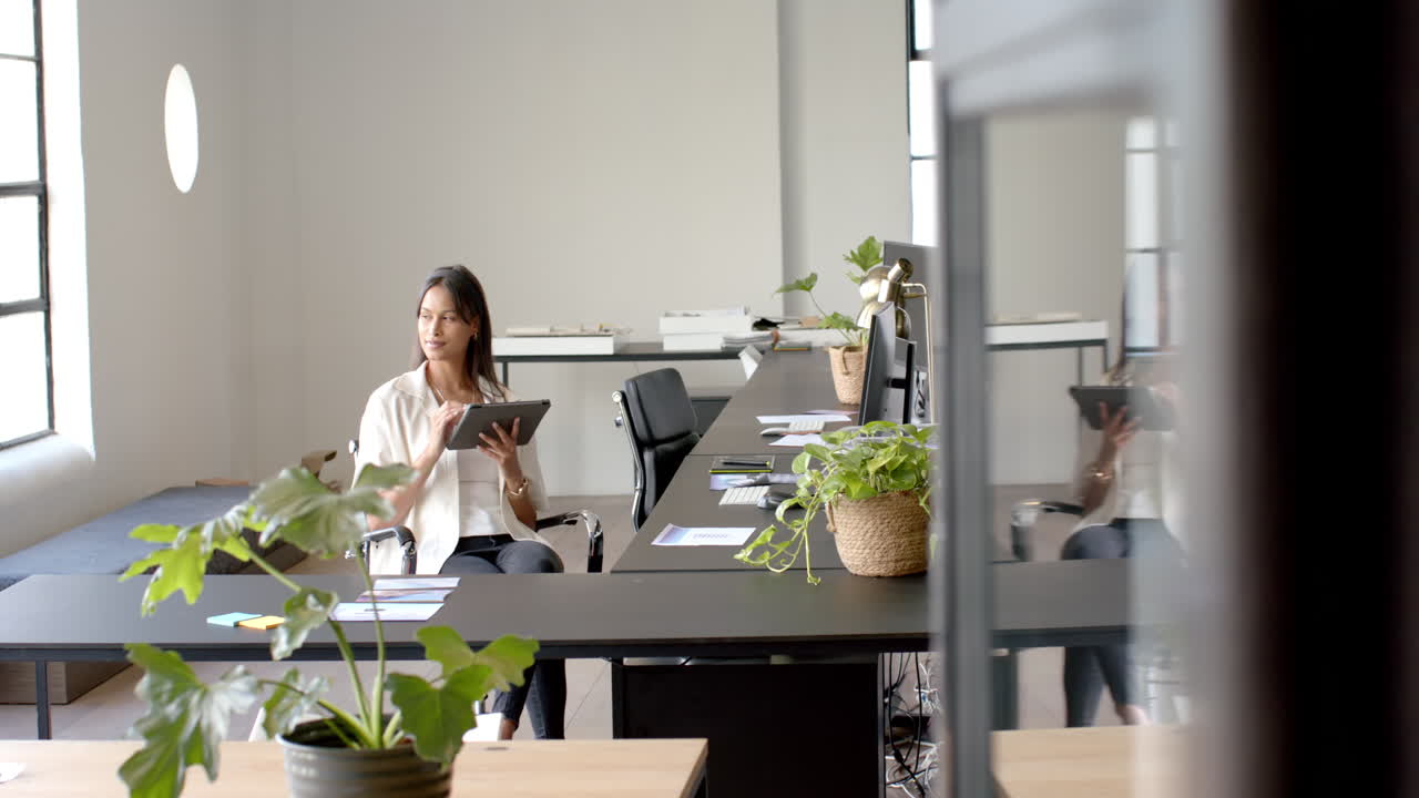 Using digital tablet, woman sitting at desk in modern office workspace