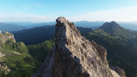 Vista-Aérea-Que-Captura-Una-Escarpada-Aguja-De-Dolomita-En-Primer-Plano,-Con-El-Icónico-Pico-Peitlerkofel-Emergiendo-Con-Gracia-En-El-Fondo-Distante-En-Medio-Del-Amplio-Panorama-Alpino