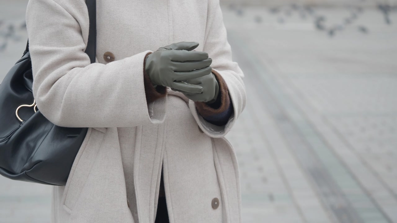 Woman in Beige Coat Adjusting Green Gloves on a Cold Day