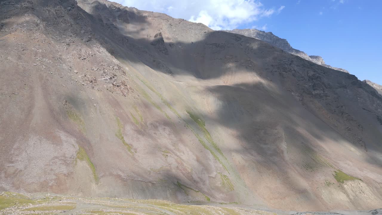 Shadows of drifting clouds dance across the side of a enormous mountain