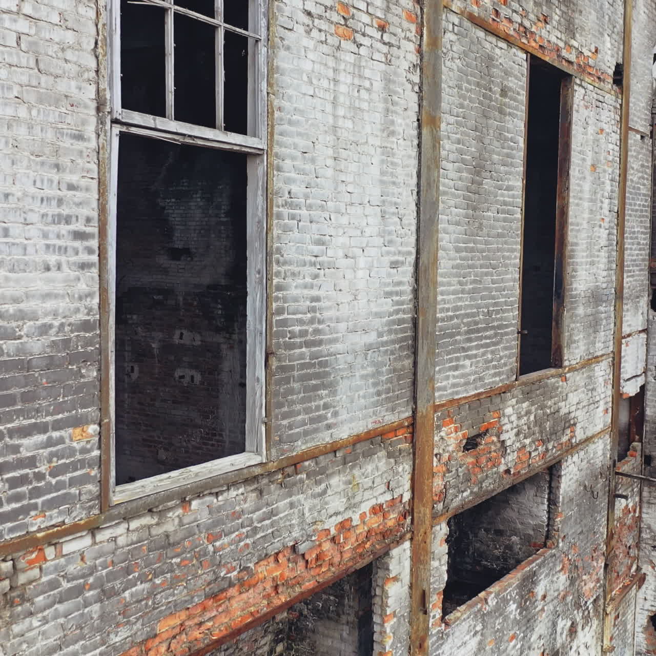 Damaged brick building without windows after the war. Close view of a destructed house with many holes in the wall. Camera moves top down
