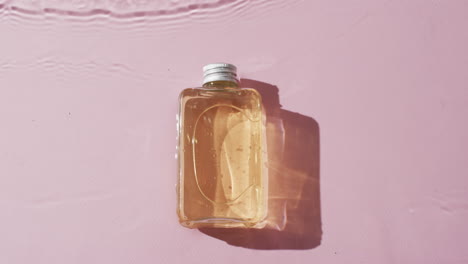 video de una botella de producto de belleza en agua con espacio de copia en fondo rosa