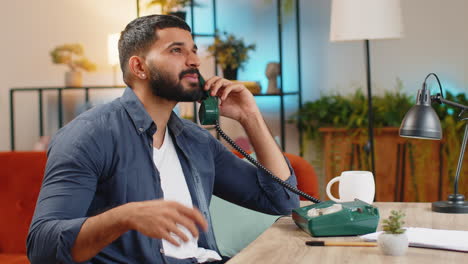 Indian-man-freelancer-working-talking-with-client-on-retro-old-fashioned-wired-telephone-at-home