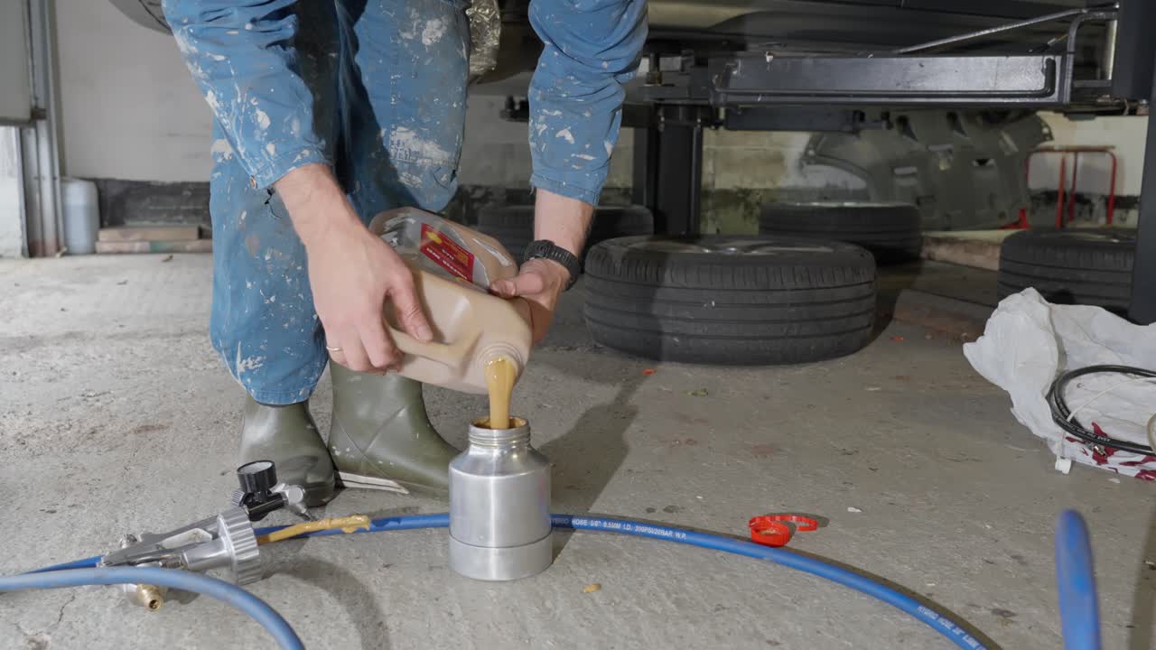 Man refills metal spray gun container with lanolin rust prevention product to spray on underside of car