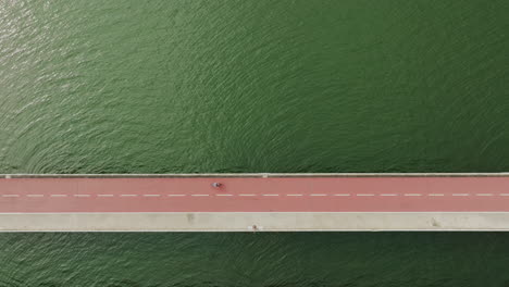 aerial top down of red asphalt bridge connecting city with pedestrian cyclist and cars crossing the water