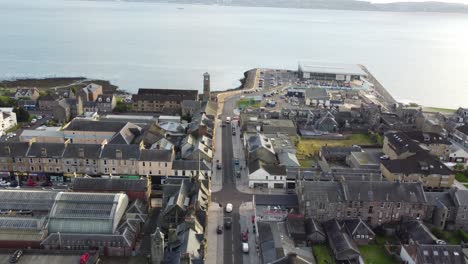 Vuelo-Sobre-Una-Calle-Con-Coches-Circulando-Por-Ella-En-El-Pueblo-De-Helensburgh-Con-Vistas-Al-Mar