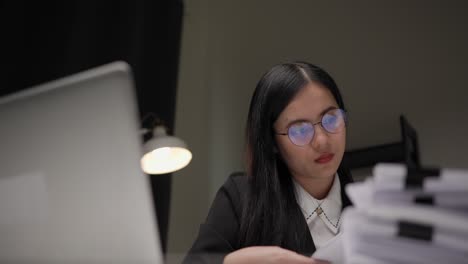 young asian business woman working at late night. she was very busy checking paperwork and had to send the work before the deadline, feeling stressed. sitting in the dark office at night.