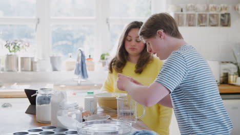 una pareja de jóvenes con síndrome de down rompiendo huevos para una receta de pastel que están horneando en la cocina en casa.