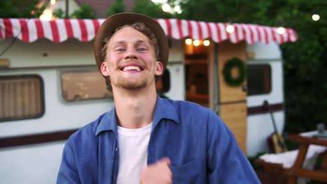 portrait d'un homme souriant à pleines dents dans des vêtements décontractés et un chapeau d'été danse à l'extérieur devant le camion remorque