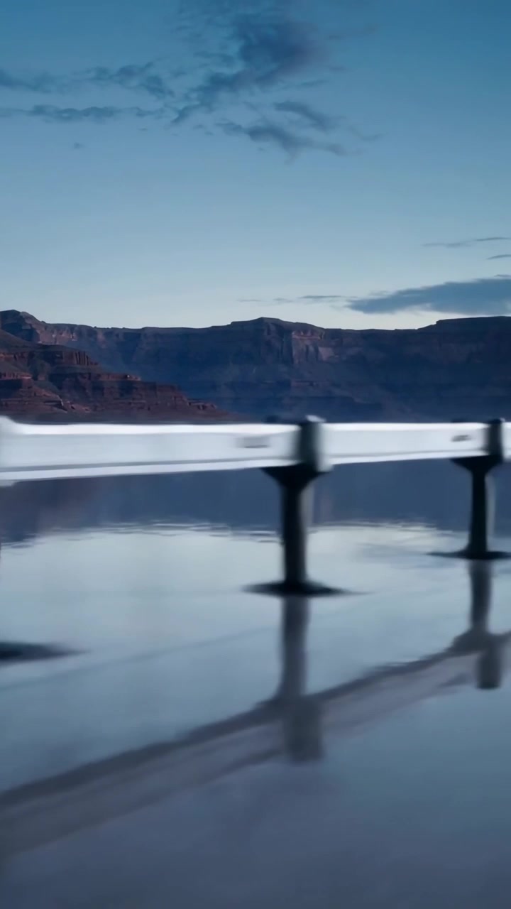 Vertical video: Sliding camera showing rail sliding across wet pavement at lake reflecting posts