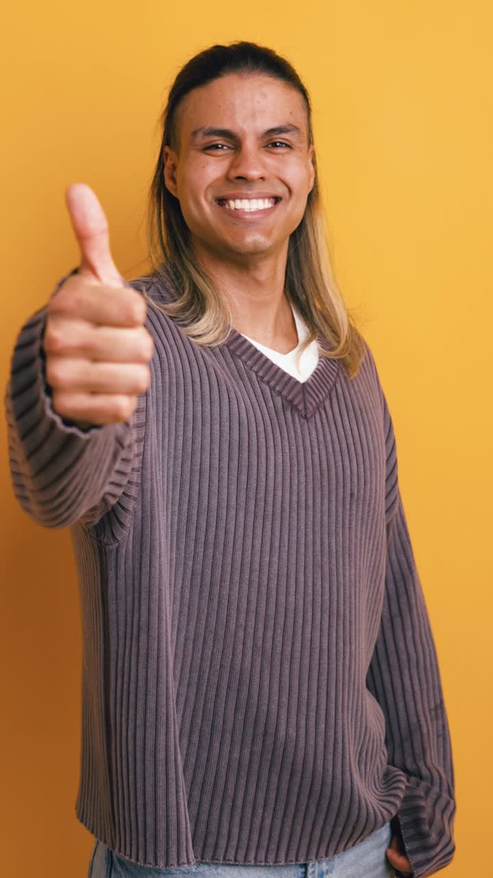 Joven sonriente haciendo un gesto de pulgar hacia arriba sobre fondo amarillo