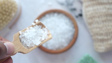 close up of white bath salts in a wooden spoon with a wooden bowl of bath salts in the background