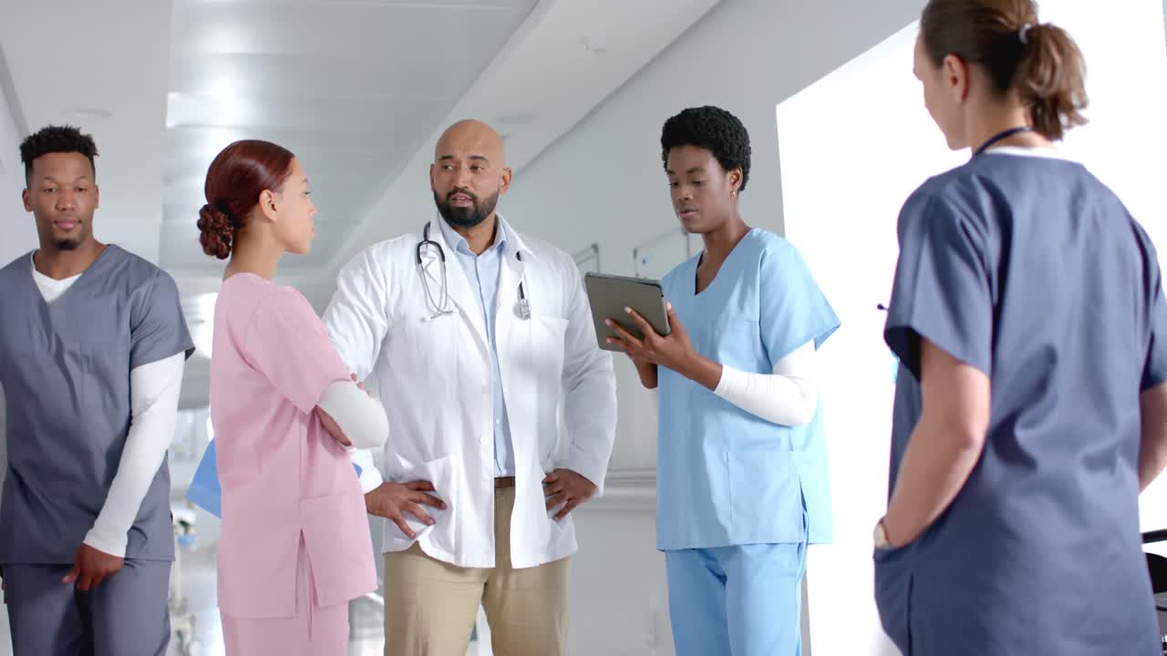 Diverse doctors discussing work and using tablet in corridor at hospital, slow motion