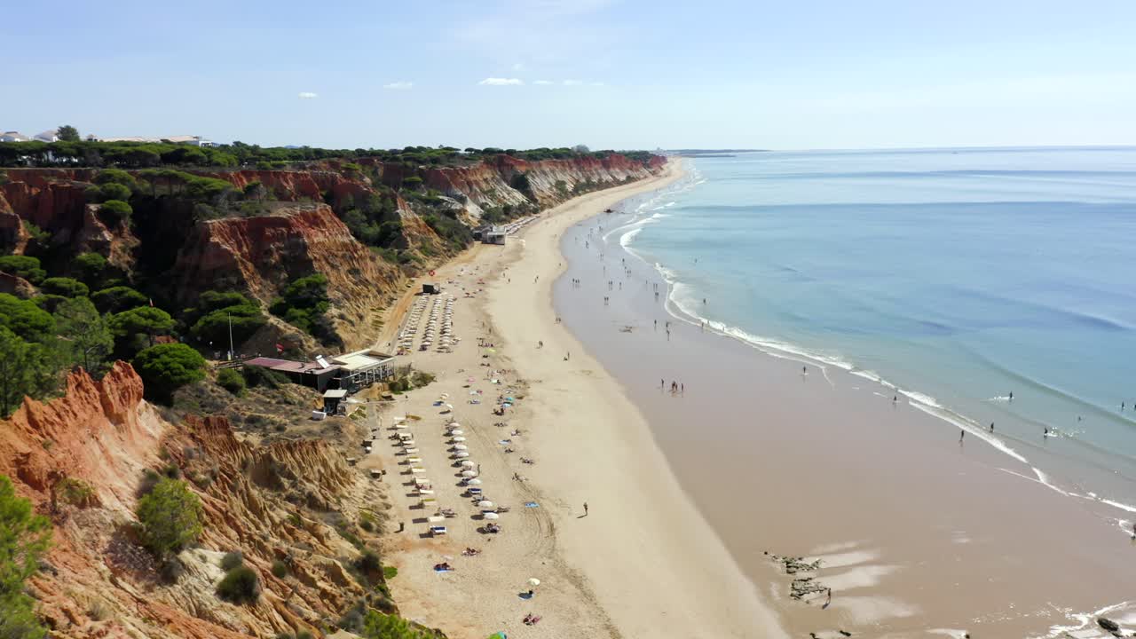 increíble playa dorada y acantilados anaranjados en portugal con aguas turquesas y olas tranquilas que se estrellan contra los turistas que disfrutan del calor