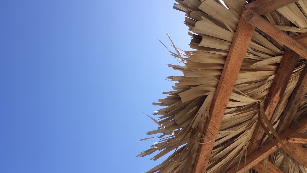 paraguas de playa de paja en una ligera brisa, vacaciones bajo un cielo azul
