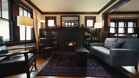 a wide push in of a cozy living room inside of a home with a beautiful brick mantle, gas fireplace, leather chairs, and a couch, all inside of a home with wooden floors