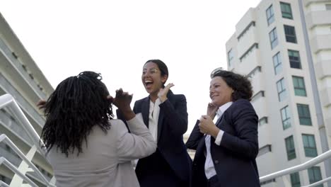 successful women laughing and giving high five on overpass