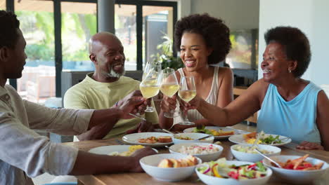 Family-Shot-With-Senior-Parents-And-Adult-Offspring-Around-Table-At-Home-Doing-Cheers-Before-Meal