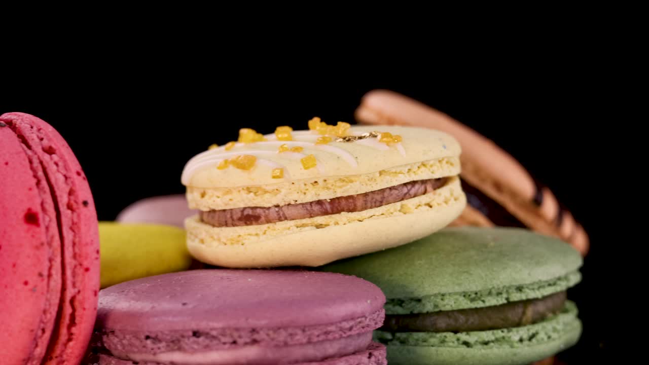 Colorful French macarons rotate on black background, showcasing vibrant shells and delicate textures