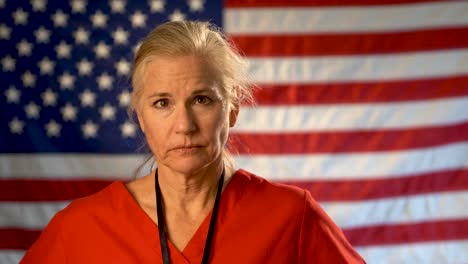 female nurse walking from out of focus us flag to a medium tight portrait looking very sad, worried and concerned