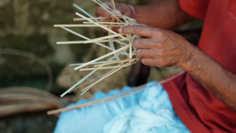 a pair of hands weaving a bamboo basket by a villager